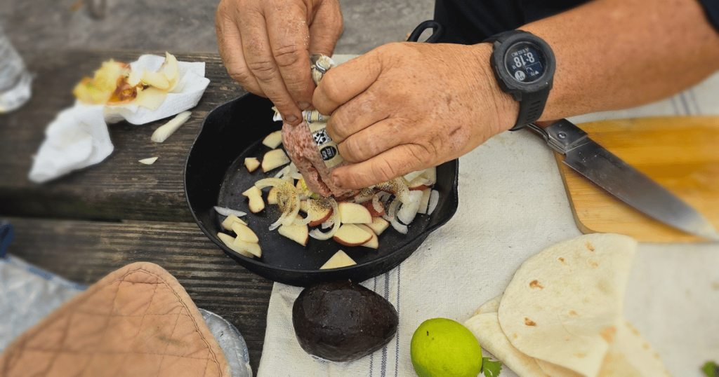 MAN ADDING POTATOES AND ONIONS TO A CAST IRON FRYING PAN