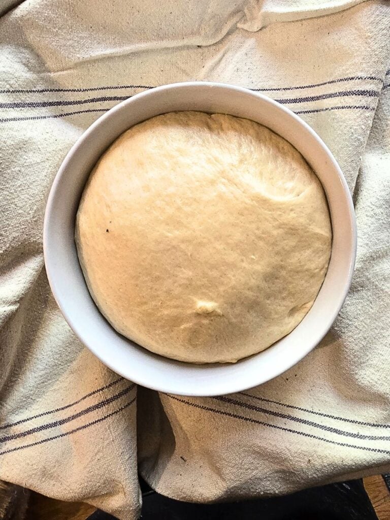 Soft cinnamon roll dough rising in a mixing bowl before baking.