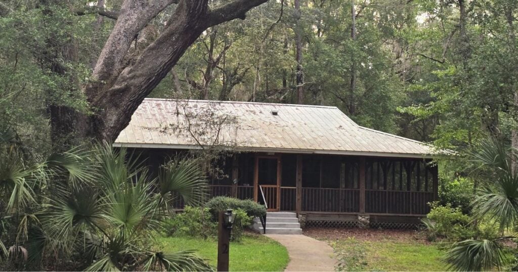 Rustic cabin in lush forest with screened porch and wooden steps.