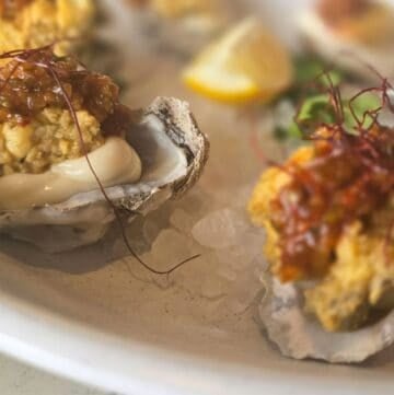 Fresh oysters topped with flavorful seafood stuffing and garnished with herbs and lemon wedges.