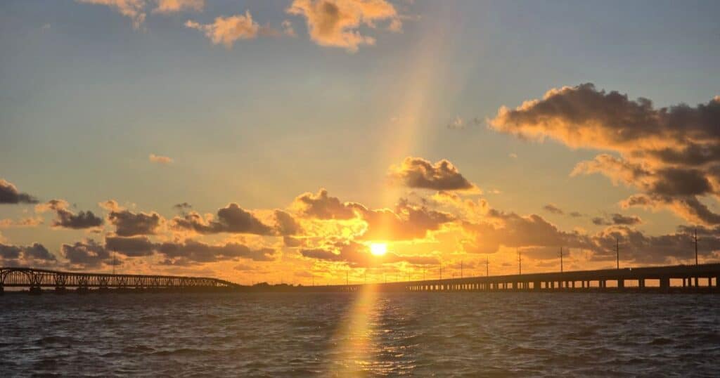 Vibrant sunset over the water with bridges and dramatic clouds, capturing a serene coastal scene.
