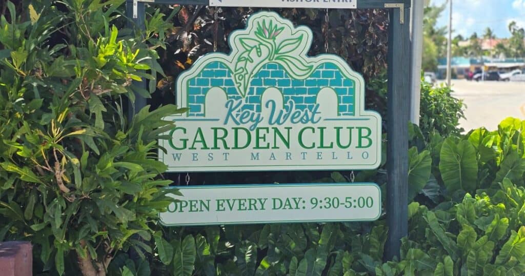 Key West Garden Club sign with lush greenery, open daily from 9:30 AM to 5:00 PM, in West Martello, Florida.