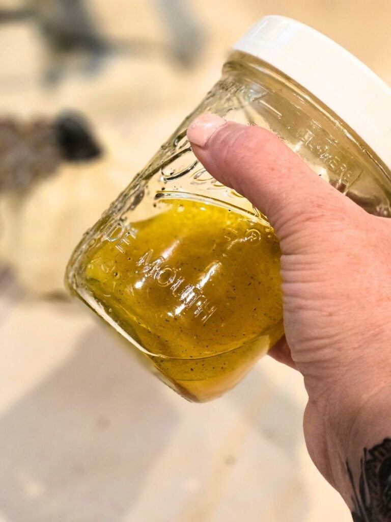 Mason jar filled with citrus vinaigrette ingredients being shaken to emulsify.
