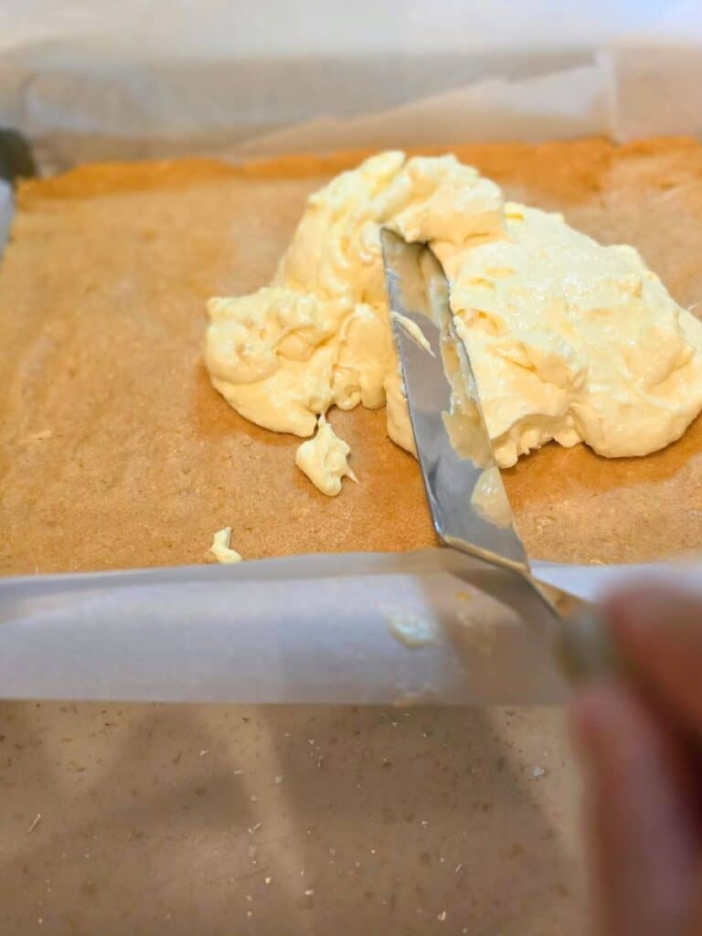 Spreading creamy filling over the crust while making smores fudge bars from scratch