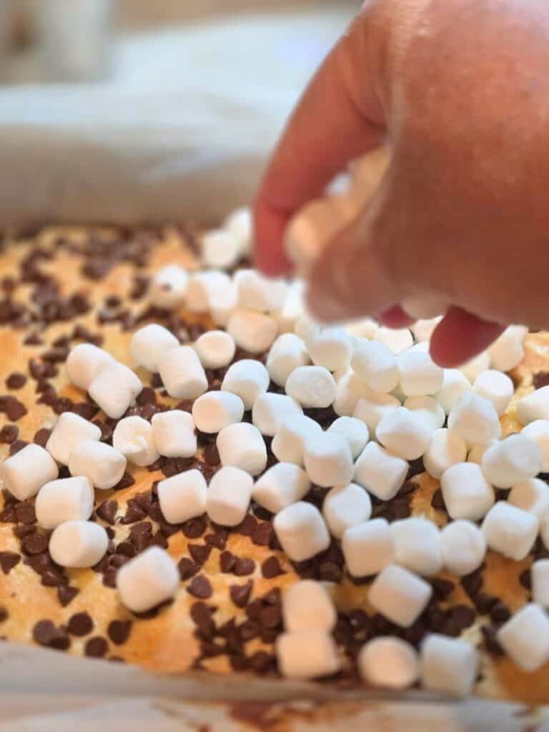 Sprinkling chocolate chips and marshmallows over the layered smores bars before baking