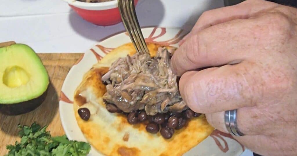 Juicy crockpot mojo pork piled on a soft tortilla ready for tacos or wraps