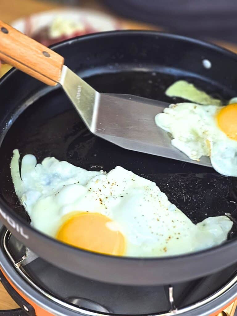 Crispy fried eggs cooking in a cast iron pan at a campsite for mojo pork tostadas, easy camping breakfast recipe with Cuban flavors and outdoor camp cooking vibes.