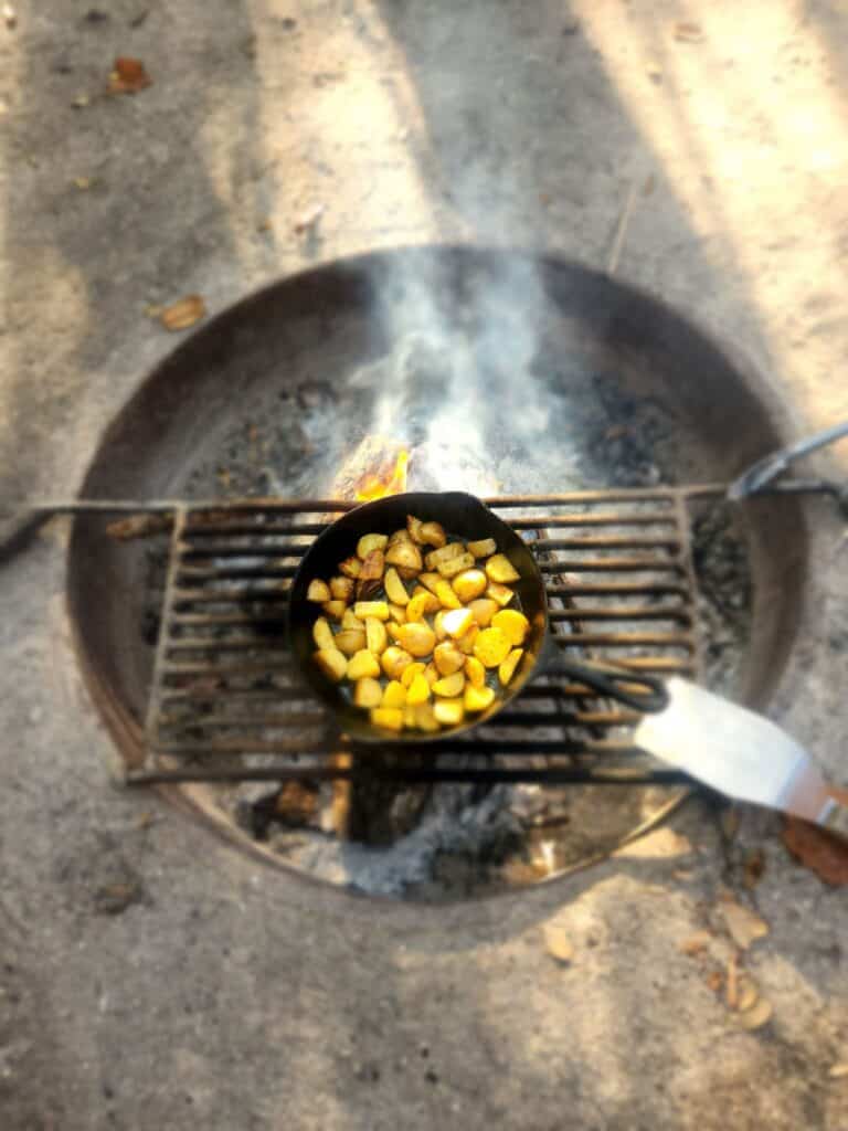 Campfire cooking at a Florida campsite with cast iron cookware over an open fire during a cozy outdoor camping adventure.